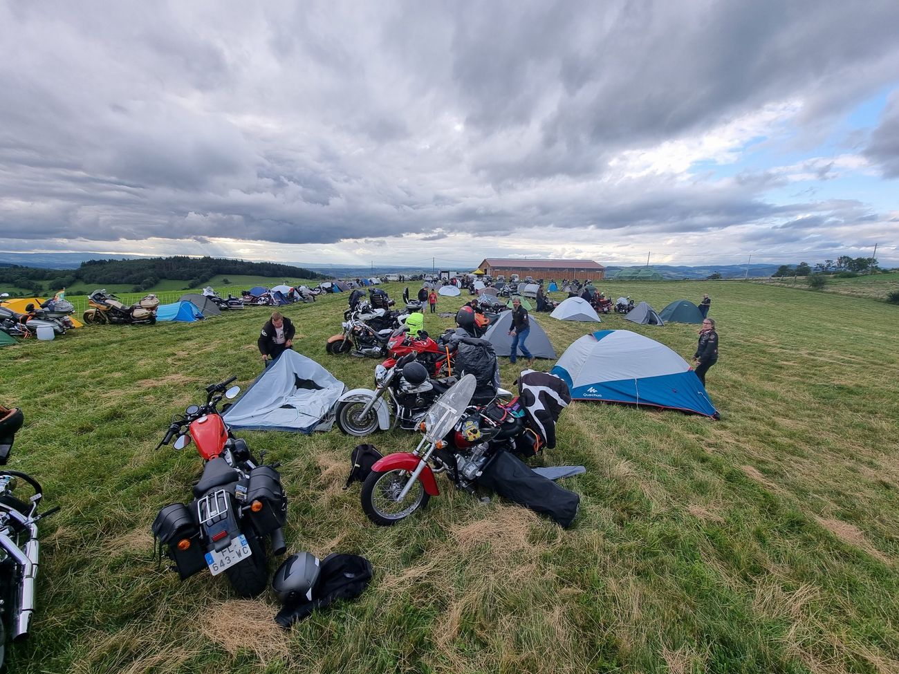 Tentes et motos dispersées dans un grand pré sous un ciel chargé