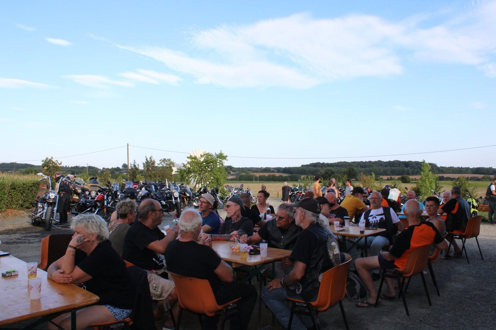 Bikers attablés en plein air au soir d'une étape, les motos garées derrière